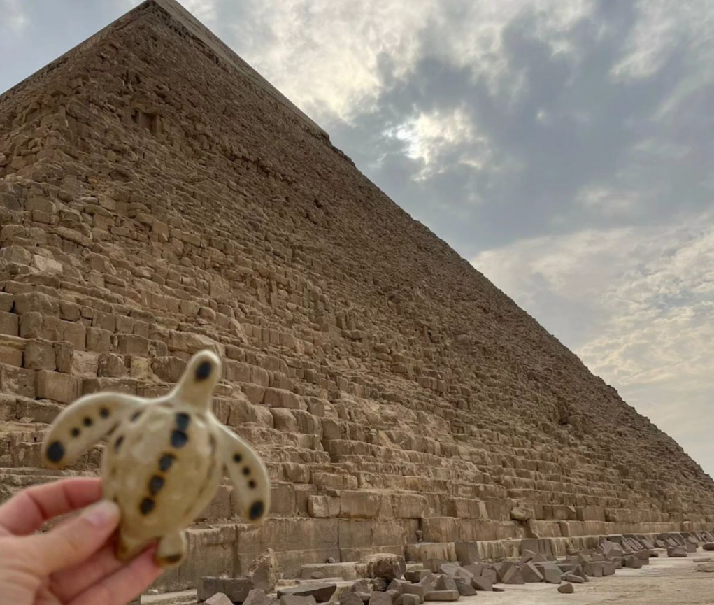 A ceramic turtle being held next to an ancient pyramid